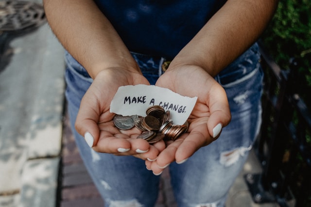 person holding out both hands which are filled with coins and a note "make a change"